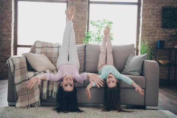 Photo of pretty funky daughter mom dressed casual clothes lying sofa upside down having fun indoors apartment room.