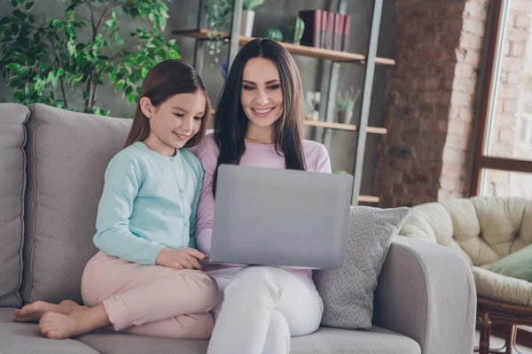 Photo of mommy sit cozy couch with kid girl use netbook browsing toy on website in modern apartment flat.