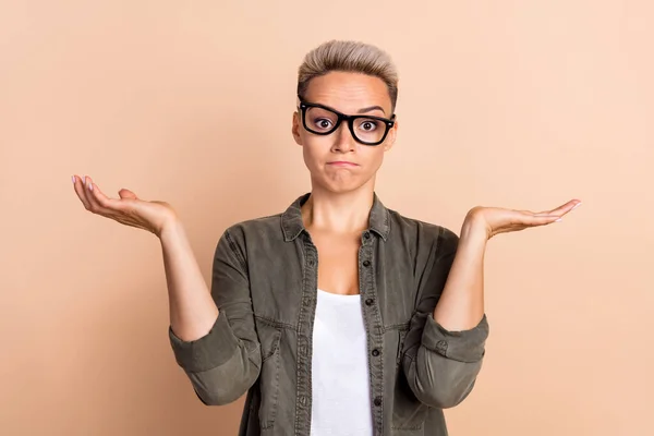 Photo of young unhappy confused woman shrug shoulders woman blonde hairstyle wear glasses no solution isolated on beige color background.