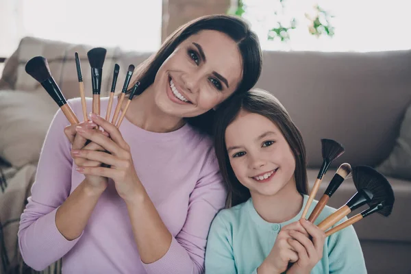 Portrait of lovely mother daughter hold brush advertise family beauty salon for preparing school party day in apartment room.