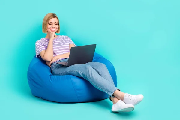 stock image Full length photo of intelligent girl dressed stylish t-shirt sit on bean bag look at laptop isolated on turquoise color background.