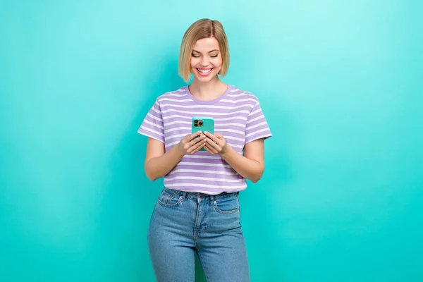 穿着条纹T恤衫的快乐女孩的照片看着智能手机在绿松石色背景下孤立地聊天 — 图库照片