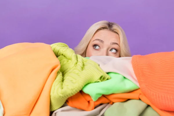 Portrait of minded person hide face behind pile stack clothes look empty space isolated on purple color background.