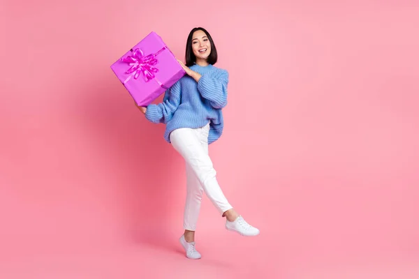 Full body portrait of pretty cheerful lady arms hold giftbox walk isolated on pink color background.