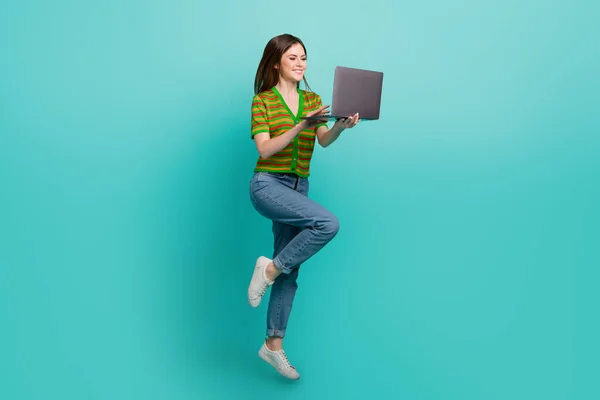 全长照片 时髦可爱的女士穿着条纹羊毛衫跳着发短信现代装置孤立的蓝绿色背景 — 图库照片