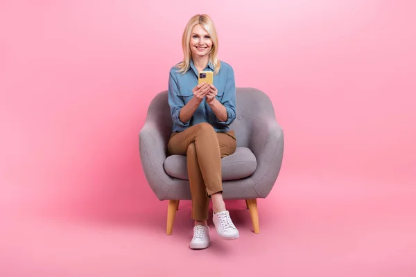 美しいビジネスの写真退職した女性が座るアームチェアは スマートフォンを使用してカジュアル服を着用ピンク色の背景を隔離 — ストック写真