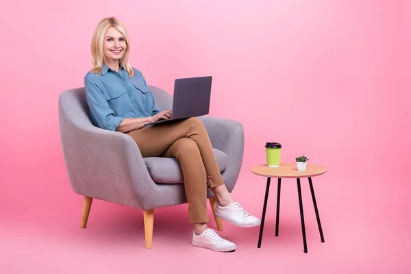 魅力的な自信のあるシニア女性労働者の写真使用ネットブック座ってアームチェアオフィスは カジュアル服を着用ピンク色の背景を隔離 — ストック写真