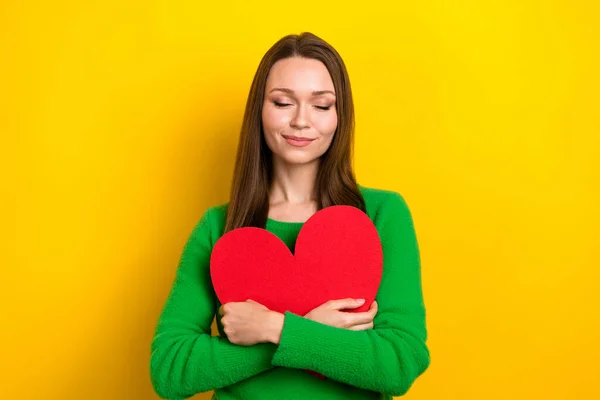 Photo of shiny dreamy woman wear green sweater embracing heart closed eyes isolated yellow color background.