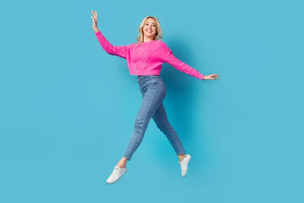 若いです背の高い女の子のステップジャンプの完全な長さ写真快適な期間月経は青の背景に隔離されたジーンズピンクのセーターを身に着けている — ストック写真