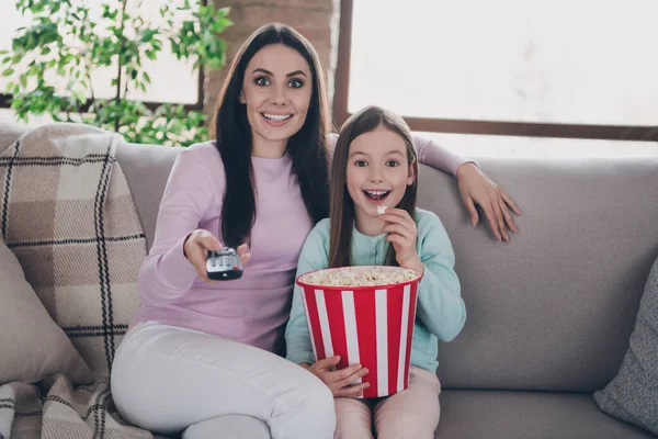 Photo of cute excited daughter mom dressed casual clothes eating pop corn watching tv indoors apartment room.