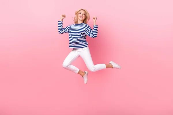 フル長さ写真の光沢のある幸運な女性の着用ストライプシャツジャンプ高上昇拳孤立ピンク色の背景 — ストック写真