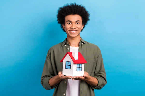 照片上 一个开朗的好人 留着卷曲的发型 穿着时髦的衬衫 抱着一幢蓝色背景的小房子 — 图库照片