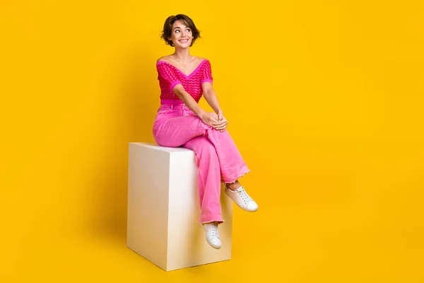 全长的神经质女人穿着粉色针织短裤坐在平台上的照片 看上去空荡荡的 与黄色背景隔离 — 图库照片