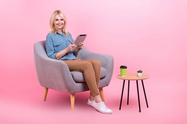 可愛い退職した女性の成功労働者の写真タブレット座ってアームチェアオフィスを使用してスマートカジュアル服孤立ピンク色の背景を身に着けて — ストック写真