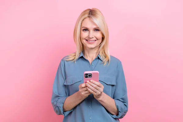 シニアオフィスワーカーの女性の写真は スマートカジュアルブラウス孤立ピンク色の背景を身に着けている現代的な技術のスマートフォンを保持 — ストック写真