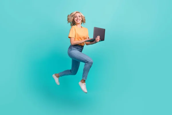 全副尺寸的照片 漂亮活泼的女孩穿着时髦的T恤衫斜纹棉裤跑动着手提电脑 用茶色背景隔开 — 图库照片