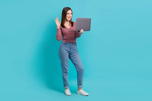 フルサイズ写真の優しい女の子身に着けているピンクカーディガンジーンズ見ますノートパソコンの手を振ってビデオ通話上の隔離された青の色の背景 — ストック写真