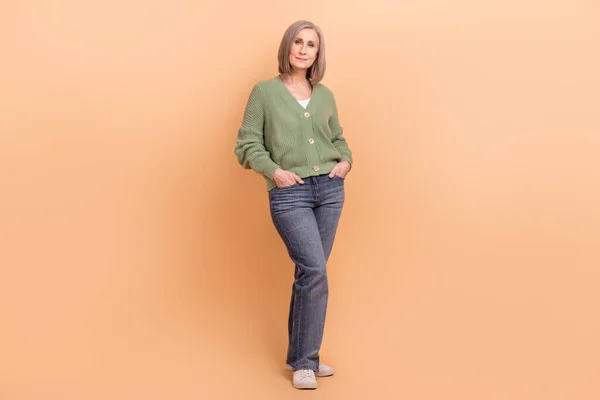 stock image Full body cadre of confident ceo manager white hair woman wear khaki cardigan hands pockets model pose isolated on beige color background.