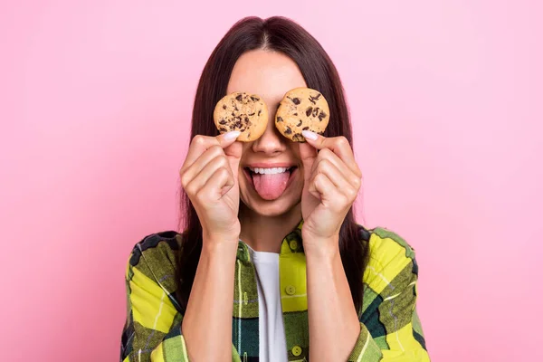 フレンドリーな人の肖像長い髪型の代わりに目の再生シャツクッキーを身に着けているピンク色の背景に隔離された舌を示す — ストック写真