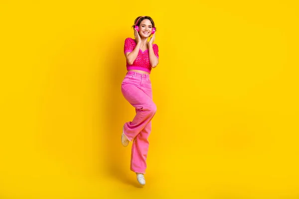 全长照片 乐观快乐的女人穿着粉色针织上衣 飘飘欲仙 带着黄色背景的耳机 — 图库照片