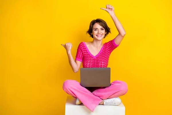 全尺寸图片 可爱女孩编织的顶部粉色裤子指示空位坐在立方体上 笔记本电脑用黄色背景隔开 — 图库照片