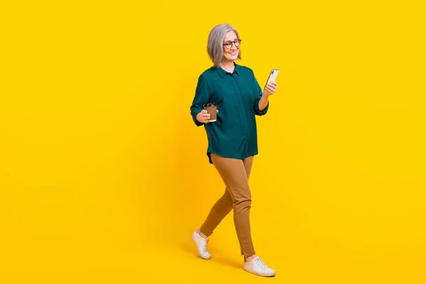 フルボディプロフィール写真のかなり人ホールドコーヒー使用スマートフォン歩行孤立で黄色の色背景 — ストック写真