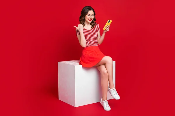 可愛い女性の完全な長さの写真スタイリッシュな服座っプラットフォームは 赤の色の背景に隔離された近代的なデバイスを購入することをお勧め — ストック写真