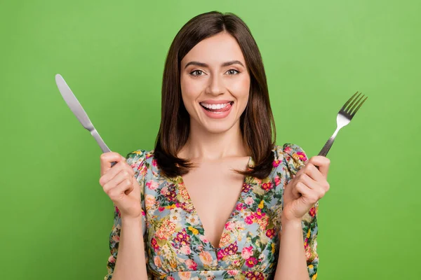 Portrait of young girl wear stylish blouse hold fork knife cutlery hungry lick teeth want eat tasty food isolated on green color background.