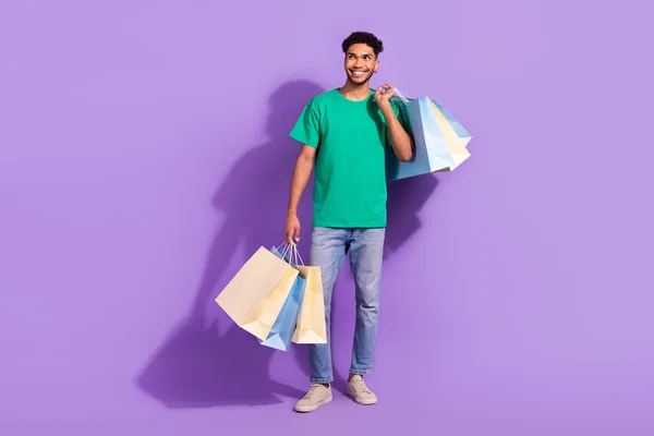 若い男のフルボディカードはTシャツホールドバッグ新しいジーンズ店見て空のスペースブランド店隔離された上に紫色の背景 — ストック写真