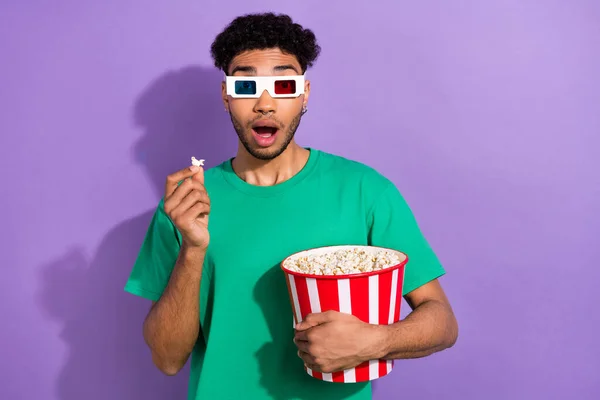 Photo of impressed shocked guy dressed green t-shirt eating pop corn watching vr film isolated violet color background.