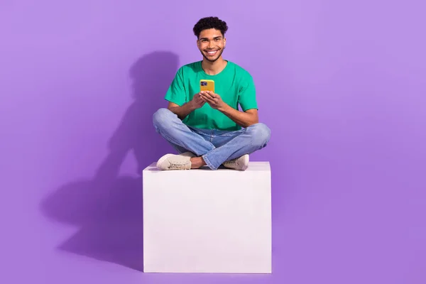 Full body photo of youth man enjoy his modern samsung smartphone four digital cameras sitting podium isolated on violet color background.