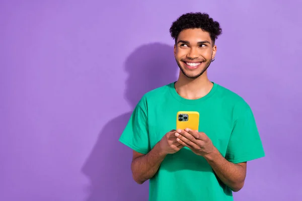 照片上积极快乐的男人穿着绿色T恤 微笑着聊天现代小玩意 空旷的空间孤立的紫色背景 — 图库照片