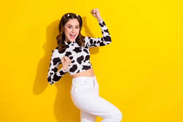 Photo of optimistic ecstatic girl curly hairdo cow long sleeve raising fists scream yes win betting isolated on yellow color background.