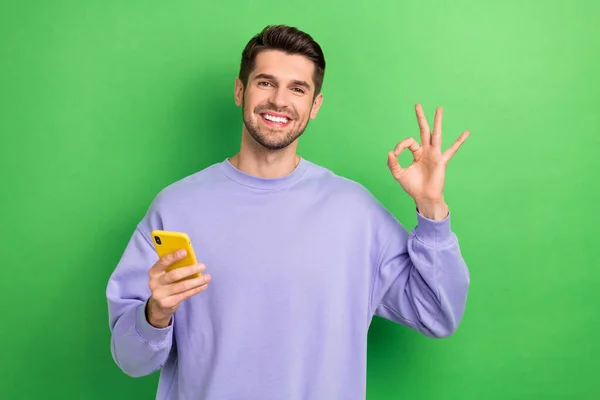 魅力的な陽気な人の肖像電話の腕の指を保持緑の色の背景に隔離されたキーシンボルを示す — ストック写真