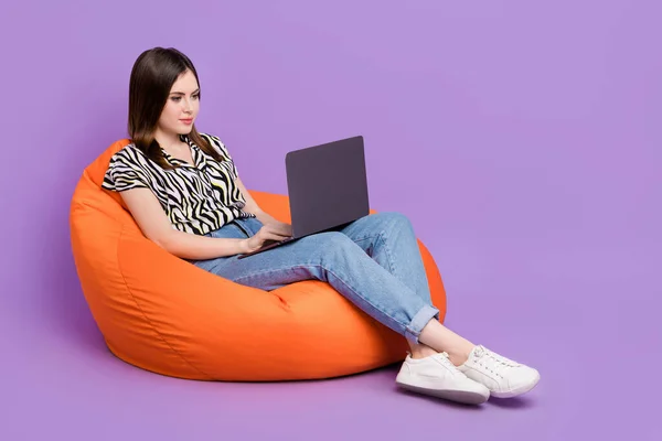 フルサイズ写真の正の美しい女の子座って居心地の良いバッグ使用無線ネットブック隔離された上に紫色の背景 — ストック写真