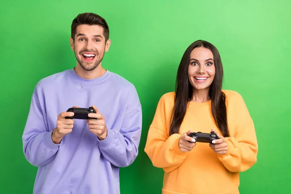 两个积极而又时髦的伴侣的肖像笑容满面 喜欢玩基于绿色背景的电子游戏 — 图库照片