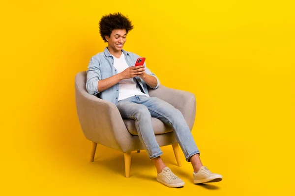 남자가 의자에 모습의 노란색 배경에 고립된 스마트폰 타이핑 포스트를 — 스톡 사진