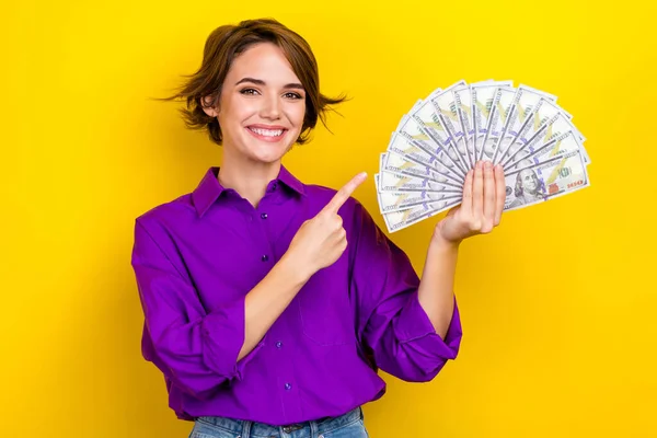 魅力的な若い女性の写真の肖像画ポイントお金のファンは黄色の色の背景に孤立スタイリッシュな紫スマートカジュアル服を身に着けている — ストック写真
