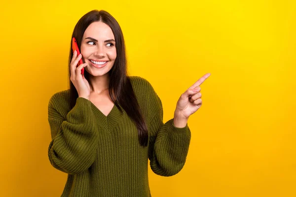 Portrait of charming lady speak communicate telephone direct finger empty space isolated on yellow color background.