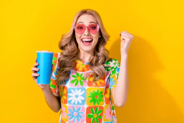 写真幸せな女性ドリンクソーダカップ喜んで格安映画価格着用ハートサングラスプリントシャツ隔離された黄色の背景 — ストック写真