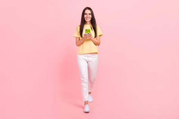 かわいいです女性の完全な長さ写真は黄色Tシャツ歩く通信現代的なガジェット隔離されたピンク色の背景 — ストック写真