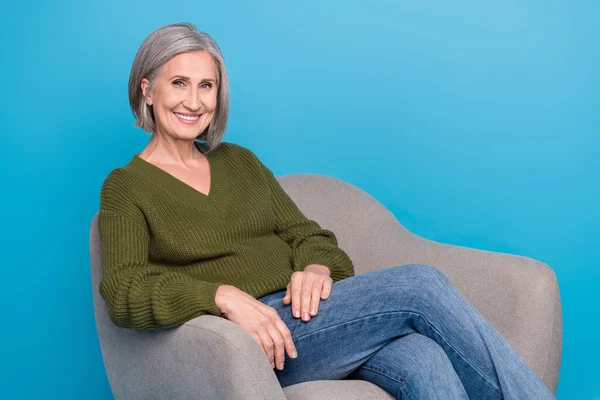 成熟した年齢の女性の写真グレーの髪の摩耗カーキセーターは 青の色の背景に隔離された精神療法のための灰色のアームチェア快適室に座る — ストック写真