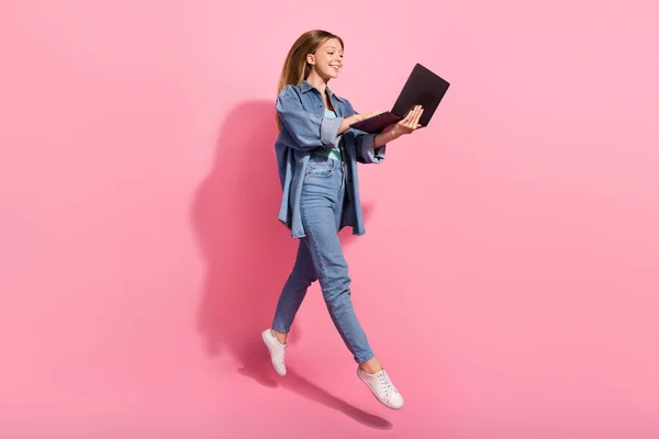 美しい女の子の写真流行の服を着て飛ぶ空気行くステップショップピンクの色の背景に隔離された近代的な技術のネットブックを使用して歩く — ストック写真