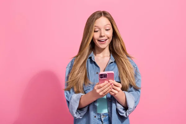 豪華な興奮した女の子の肖像は流行の服を着てピンクの色の背景に隔離された現代の電話のIphoneの読書Facebookのニュースを使用 — ストック写真