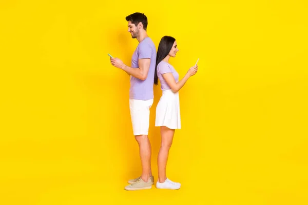 年轻漂亮女孩的全身照片 男人背对背拿着电话发短信 穿着时髦的紫色衣服 背景是黄色的 — 图库照片