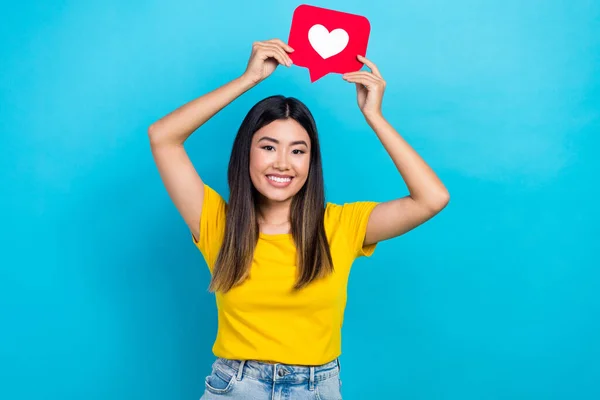 若い影響力のある女性の写真ブログホールド赤ハート通知クリックアイコンは 青の色の背景に隔離された黄色のTシャツを着用 — ストック写真