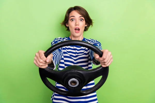 照片中 滑稽兴奋的女孩穿着条纹T恤衫 手握方向盘 突如其来的车祸发生在绿色背景下 — 图库照片