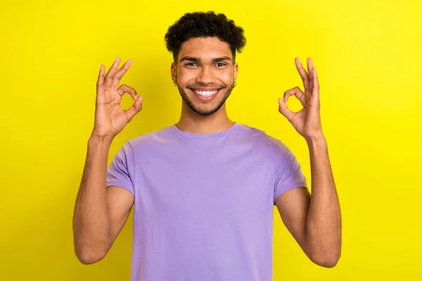 写真のファンキーな自信を持った男の服を着て紫のTシャツ笑顔を示す2つの主要なジェスチャー孤立した黄色の背景 — ストック写真