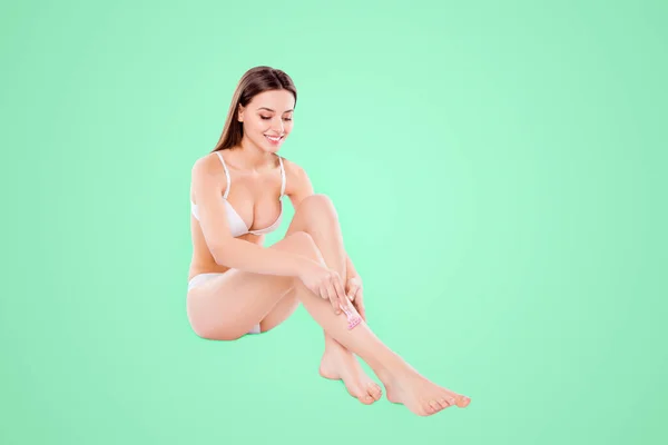 白い背景の上に座って慎重にほっそりした長い脚を剃るきれいな女性の肖像画 — ストック写真
