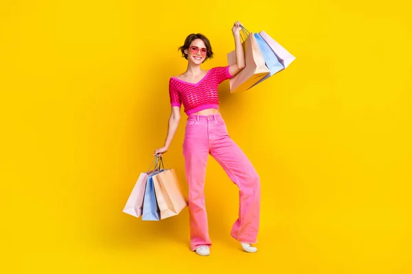 Full body photo of hipster girl bob brown hair wear stylish pink crop top trousers hold many shopping bags isolated on yellow color background.